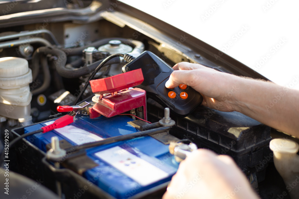 Car battery repair and inspection. The man measures the voltage and capacity of the battery with a tester. Car service Car battery repair and inspection. The man measures the voltage and capacity of the battery with a tester. Car service