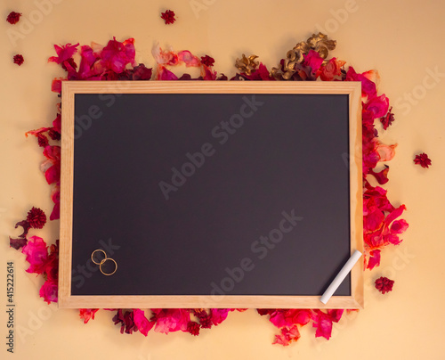 Pizarra sobre fondo de flores con anillos de boda
