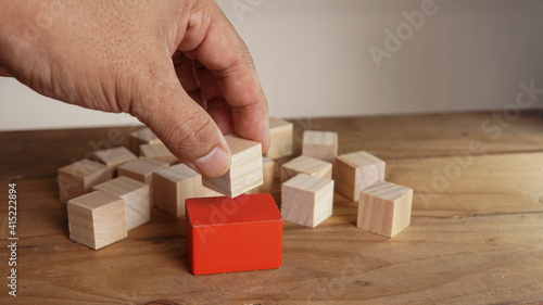 Man hand placing wooden block on a red block around another wooden block. Nomination concept.