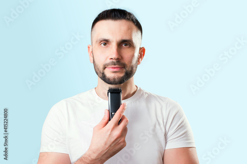 Man shaves his beard with a trimer on a blue background