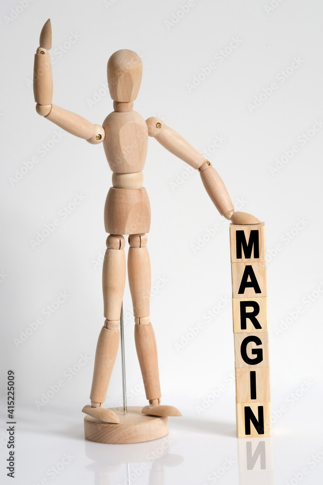 The wooden man raised his hand, and under his left hand he has cubes with the inscription - MARGIN The wooden man raised his hand, and under his left hand he has cubes with the inscription - MARGIN