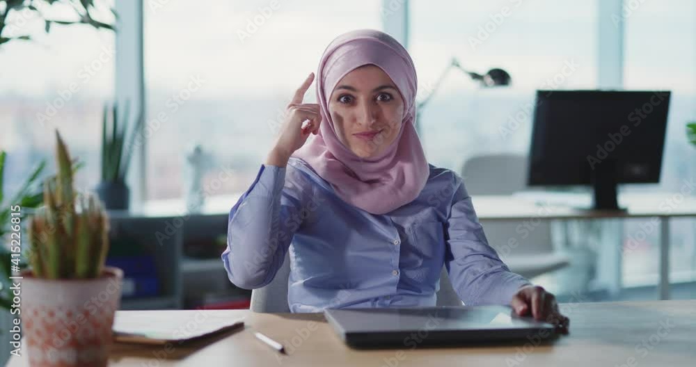Positive pretty young arabic business woman showing her finger near brain gesturing at camera. Face expressions. Muslim manager. Corporate office. Positive pretty young arabic business woman showing her finger near brain gesturing at camera. Face expressions. Muslim manager. Corporate office.