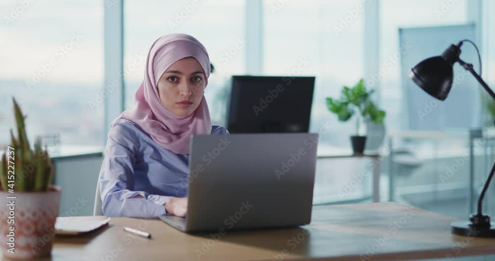 Muslim arabic young office executive female weairng hijab and smiling to camera working by laptop. International office. Arab businesswoman. Muslim arabic young office executive female weairng hijab and smiling to camera working by laptop. International office. Arab businesswoman.