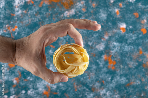 Male hand holding tagliatelle nest on colorful background