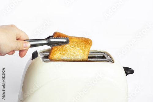 Close up of a toasted fresh delicious toast in an ivory-colored toaster for breakfast on a white background. A woman takes out a hot toast with a special tool. Delicious breakfast. Template fot design