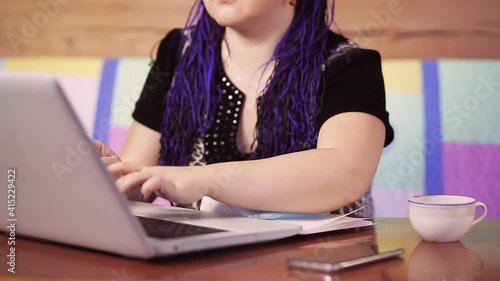 Young woman with blue afrokos at home on the couch works with a laptop without a face photo