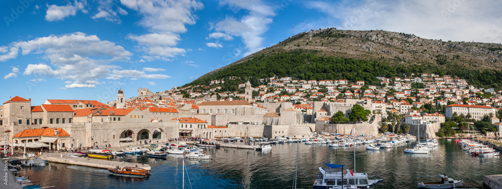 Beautiful view over the harbor and city walls of Dubrovnik's medieval centre under a blue sky with clouds. Dalmatia, Croatia.