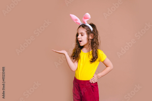 Pretty blonde girl child with rabbit ears looks at her palm in surprise. Traditions, discounts, medicine, the concept of the celebration.