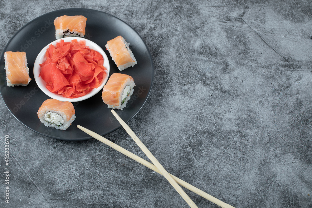 Salmon sushi rolls served with red ginger on a black plate Salmon sushi rolls served with red ginger on a black plate