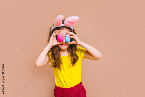 Cute girl child with Easter bunny ears holds a basket of colored eggs. Happy Easter, holidays, traditions concept.