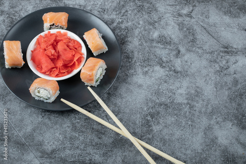 Salmon sushi rolls served with red ginger on a black plate