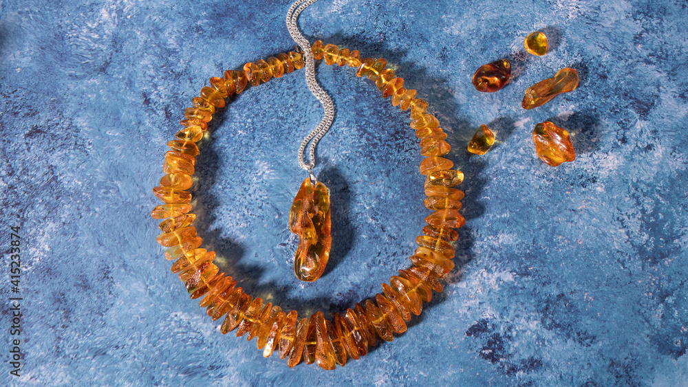 Fototapeta premium Amazing transparent orange amber pendant and necklace on a blue background. Retro composition, flat lay, copy space. 