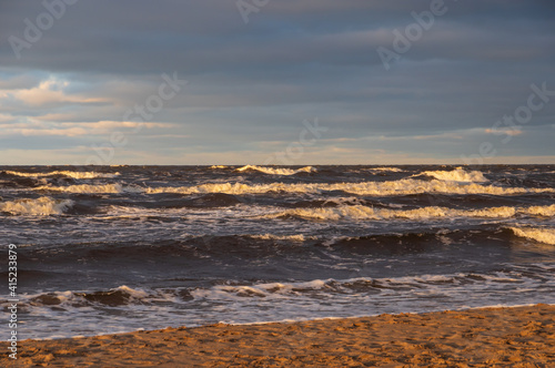 Wavy water of the Baltic sea and sandy shore in the warm evening sunlight 