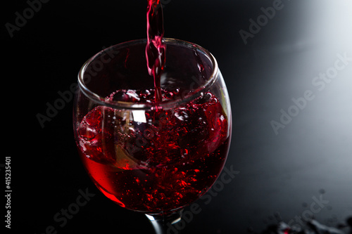 Pouring red wine with splashes and drops into a glass on a black background.