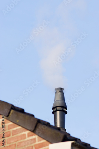 Closeup of a chimney system of a house with smoke and a clear blue sky
