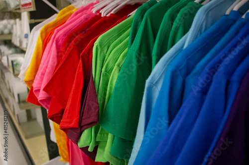 A view of several t-shirts organized in a rainbow color motif, hanging in a retail store.