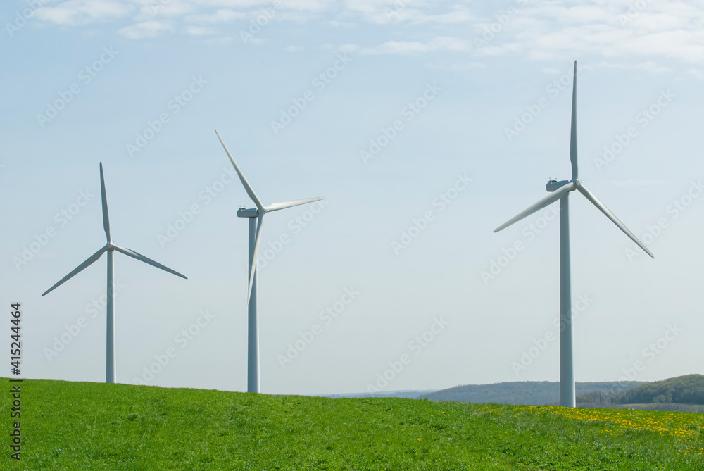 three wind towers rise up from behind a green field three wind towers rise up from behind a green field