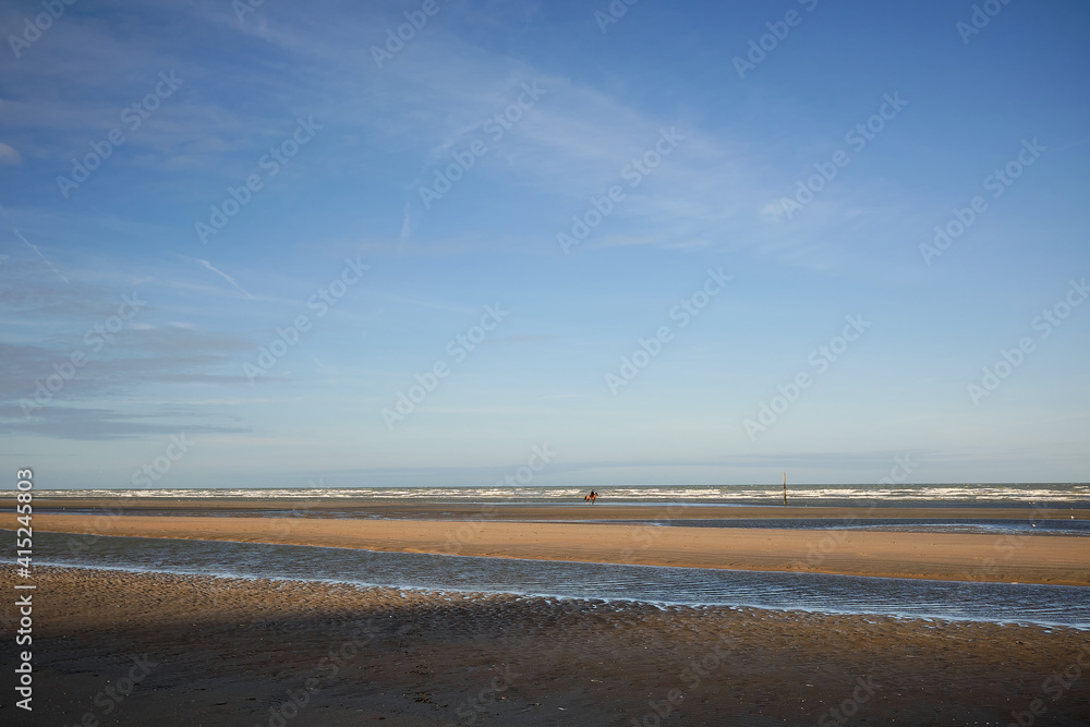 A person is riding a horse by the Flemish coastline, the beach of the North Sea is completely abandoned