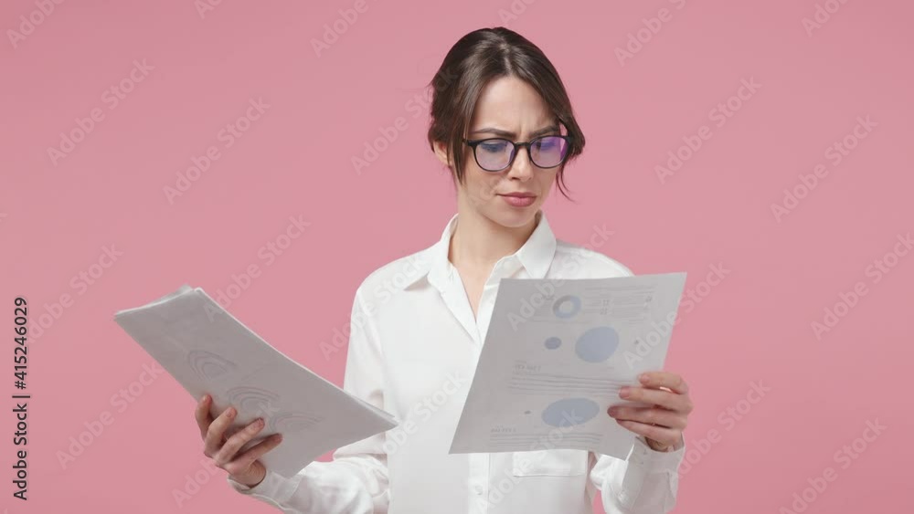 Excited joyful young business woman in white shirt glasses isolated on pink background studio. Achievement career wealth concept. Work with financial statistics papers documents doing winner gesture Excited joyful young business woman in white shirt glasses isolated on pink background studio. Achievement career wealth concept. Work with financial statistics papers documents doing winner gesture