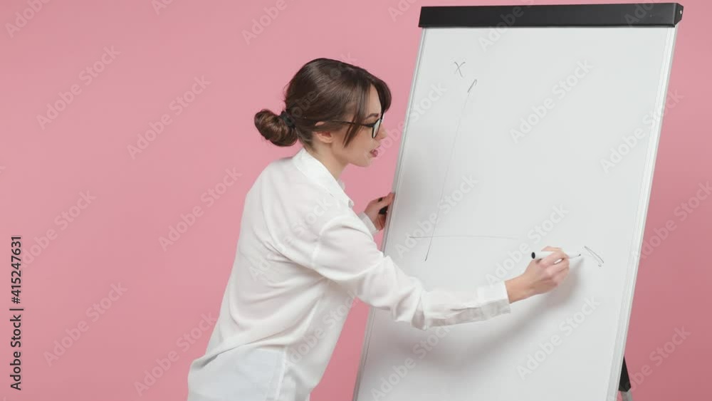 Excited business woman speaker in shirt glasses isolated on pink background studio. Achievement career concept. Talking presentation strategy plan showing statistics drawing graphs on flip chart board Excited business woman speaker in shirt glasses isolated on pink background studio. Achievement career concept. Talking presentation strategy plan showing statistics drawing graphs on flip chart board