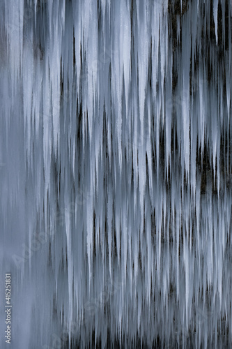 Beautiful long icicles of a frozen waterfall  with water flowing and crashing down and Ice water dripping from the tips of icicles in a cold eery and moody atmosphere in a cave in the mountains 