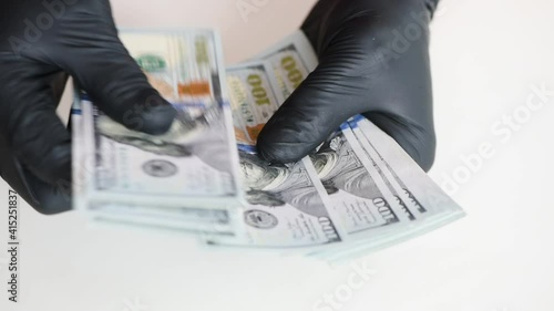 Hands in black gloves are counting money. One hundred US dollar bills.