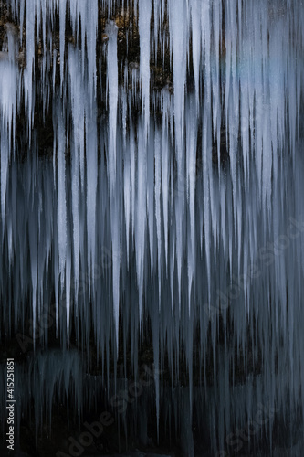 Beautiful long icicles of a frozen waterfall  with water flowing and crashing down and Ice water dripping from the tips of icicles in a cold eery and moody atmosphere in a cave in the mountains 