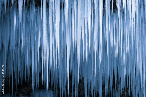 Beautiful long icicles of a frozen waterfall, with water flowing and crashing down and Ice water dripping from the tips of icicles in a cold eery and moody atmosphere in a cave in the mountains 