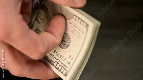 Hands are counting money. One hundred US dollar bills.