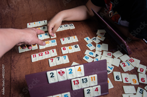 Kid playing Rummy with game tiles laid on a plastic rack simulating wood, in a mosaic style
 photo