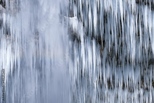 Beautiful long icicles of a frozen waterfall, with water flowing and crashing down and Ice water dripping from the tips of icicles in a cold eery and moody atmosphere in a cave in the mountains 