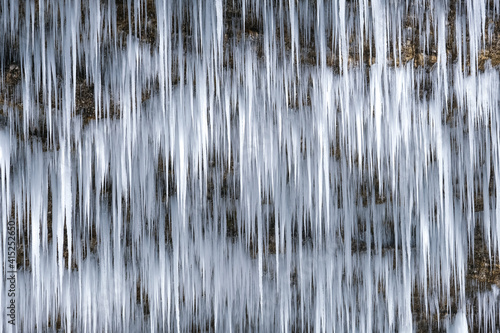 Beautiful long icicles of a frozen waterfall, with water flowing and crashing down and Ice water dripping from the tips of icicles in a cold eery and moody atmosphere in a cave in the mountains 