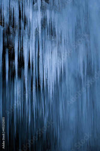 Beautiful long icicles of a frozen waterfall, with water flowing and crashing down and Ice water dripping from the tips of icicles in a cold eery and moody atmosphere in a cave in the mountains 