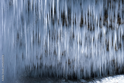 Beautiful long icicles of a frozen waterfall, with water flowing and crashing down and Ice water dripping from the tips of icicles in a cold eery and moody atmosphere in a cave in the mountains 