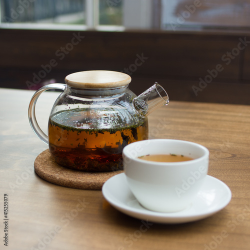 Glass teapot and white porcelain cup with tea on a wooden table. Shallow depth of field. Background blurred