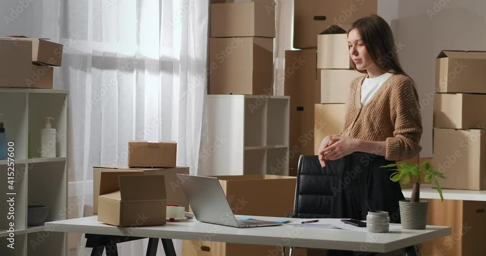 online meeting of partners by video chat in laptop, woman is speaking from warehouse with many of cardboard boxes, small company online meeting of partners by video chat in laptop, woman is speaking from warehouse with many of cardboard boxes, small company