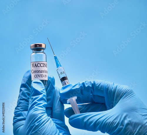 A bottle of COVID-19 vaccine and a syringe with an injection needle against coronavirus infection in the doctor's hand in a nitrile glove on a blue background. Close-up. Place to copy. The concept of