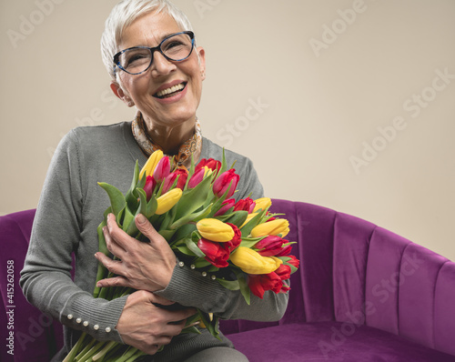 Senior female with flowers. International women's day. Senior female with short grey hair. Grandma with flowers. Happy and smiling senior lady. Celebrating valentines as a senior.