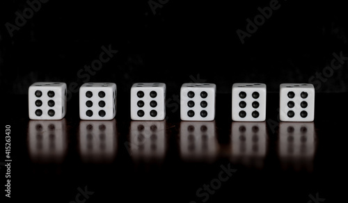 Six dice, all showing six, on a table with reflection and black background