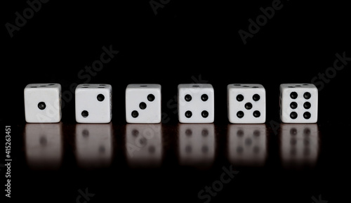 Six dice showing one through six on a table with reflection and black background