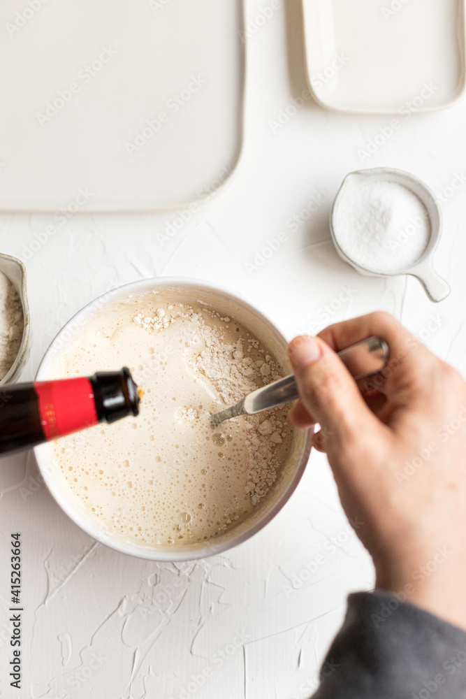 Fototapeta premium Overhead view of a hand man stirring tempura butter with a metallic spoon and dropping very cold beer on it.
