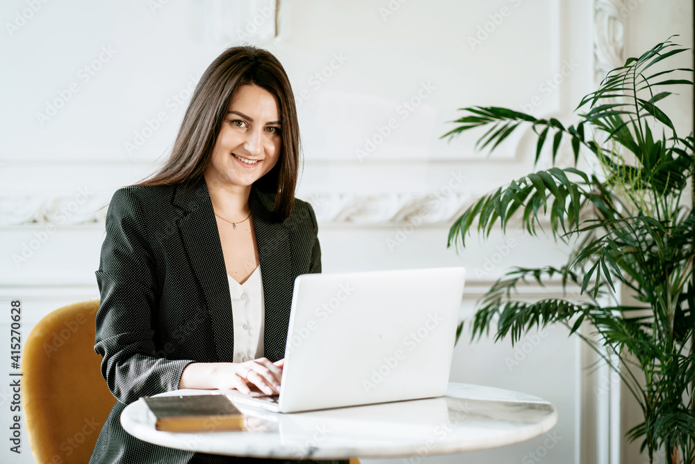 Online training in a cafe. A brunette psychologist in a business suit. Sitting in a comfortable chair and reading an electronic textbook on a laptop. The student studies the basics of economics. Online training in a cafe. A brunette psychologist in a business suit. Sitting in a comfortable chair and reading an electronic textbook on a laptop. The student studies the basics of economics.