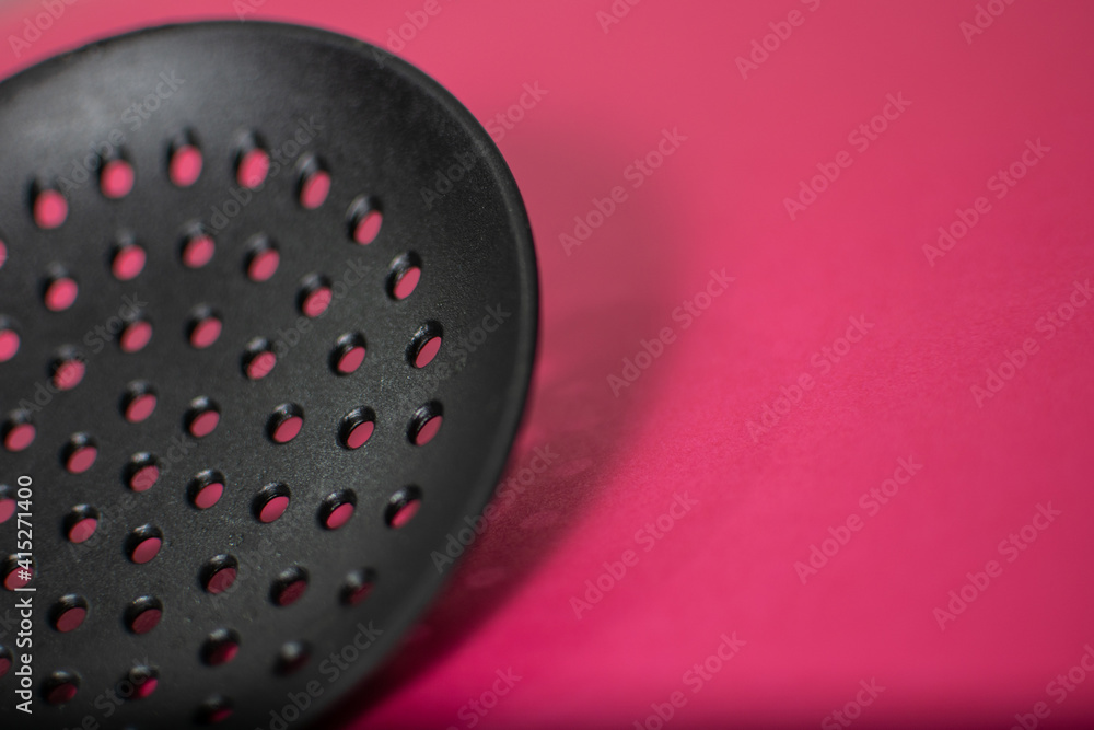 Black Plastic holed skimmer cooking spatula on pink background with space to copy
Black Plastic holed skimmer cooking spatula on pink background with space to copy