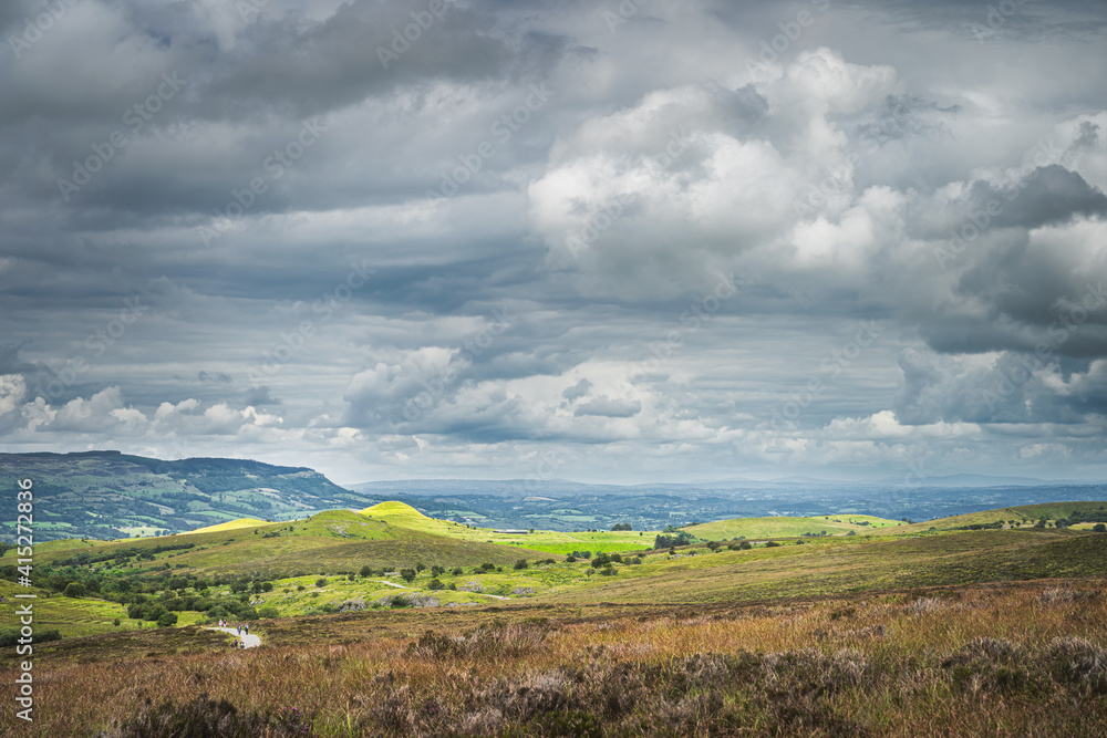 Obraz premium Green hills with pastures illuminated by patches of sunlight and stormy sky in background, Cuilcagh Mountain Park, Northern Ireland