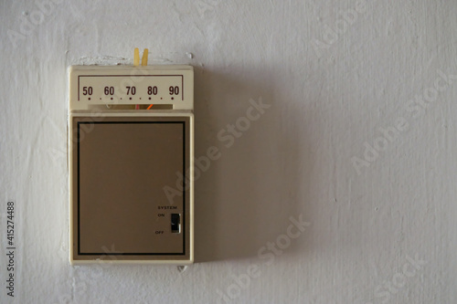 An old, analog temperature control thermostat is shown on a wall up close, with text or copy space to the right.