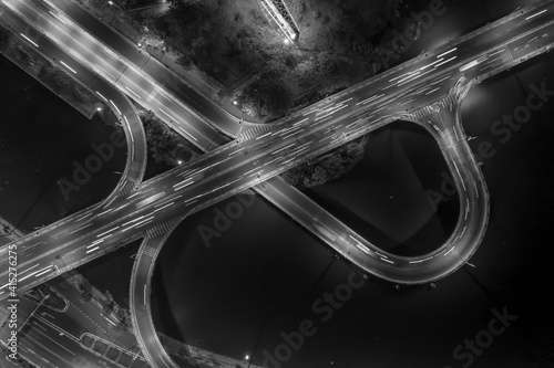 graphic drone top down shot of complex road system with interchange, traffic, bridge, ramps and loops at night over a river in Black and white. photo