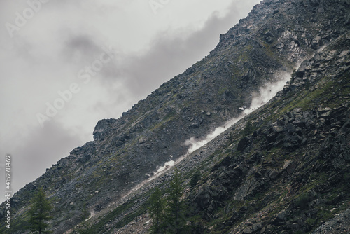 Fotografie Good shot of rockfall on rocky mountain steep slope and long trail of dust