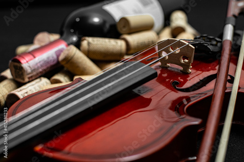 Close view of a classical small violin, strings and bridge over a dark black blanket background with wine corks and wine bottle
