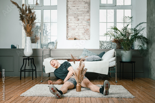 Close-up of a young man in a sports uniform is resting on the floor at home, looking at the camera and smillling on bedroom. Student loafing around and putting off work and study photo