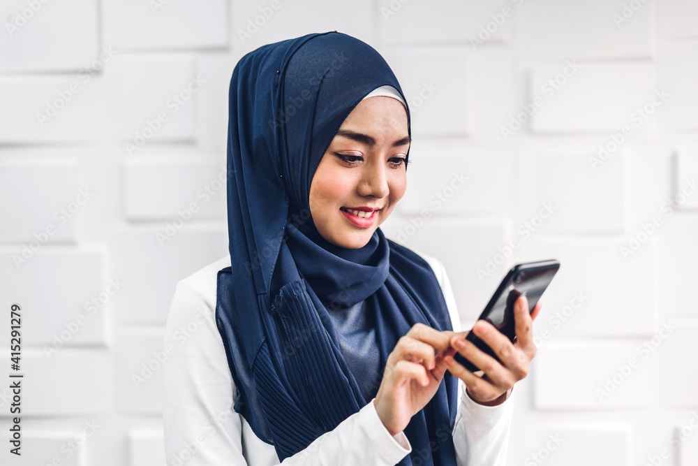 Portrait of smiling happy beautiful muslim woman relaxing using digital smartphone.Young muslim girl looking at screen typing message and playing game online or social media Portrait of smiling happy beautiful muslim woman relaxing using digital smartphone.Young muslim girl looking at screen typing message and playing game online or social media